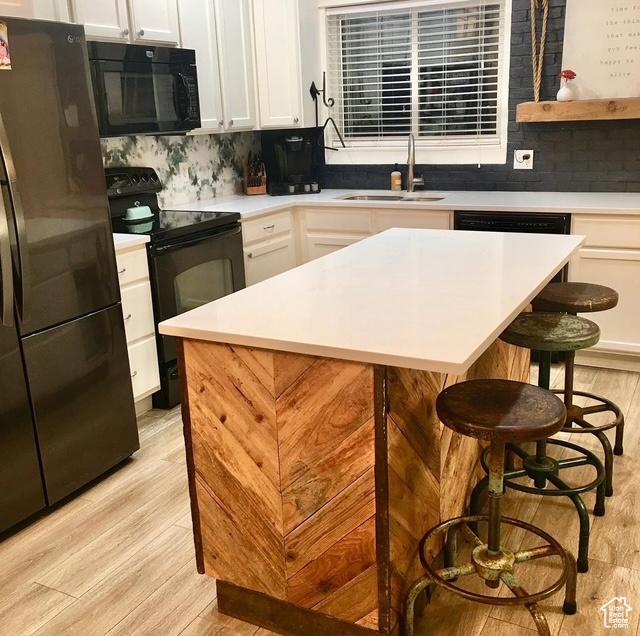 kitchen featuring black appliances, light wood-style floors, a sink, a kitchen bar, and light countertops