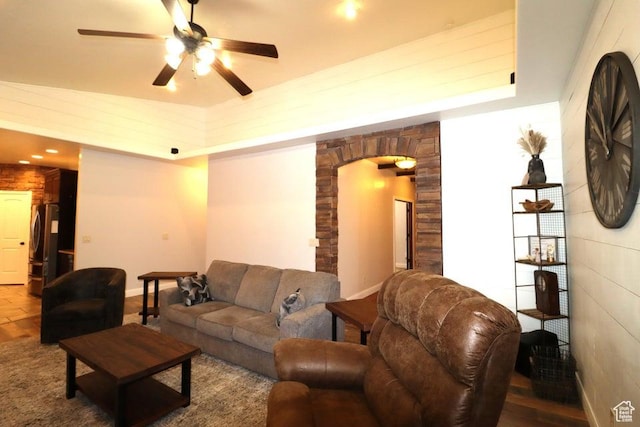 living area with a raised ceiling, arched walkways, a ceiling fan, and baseboards