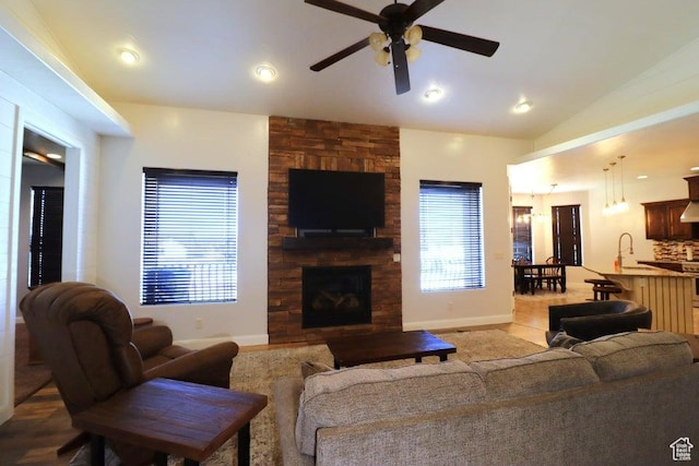 living area featuring a stone fireplace, vaulted ceiling, baseboards, and ceiling fan