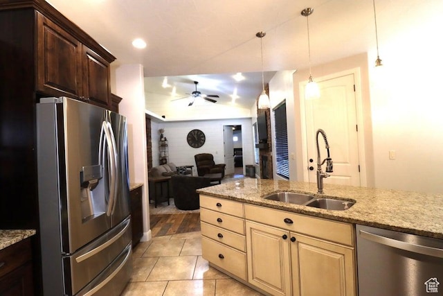 kitchen with a sink, stainless steel appliances, light stone counters, open floor plan, and a ceiling fan