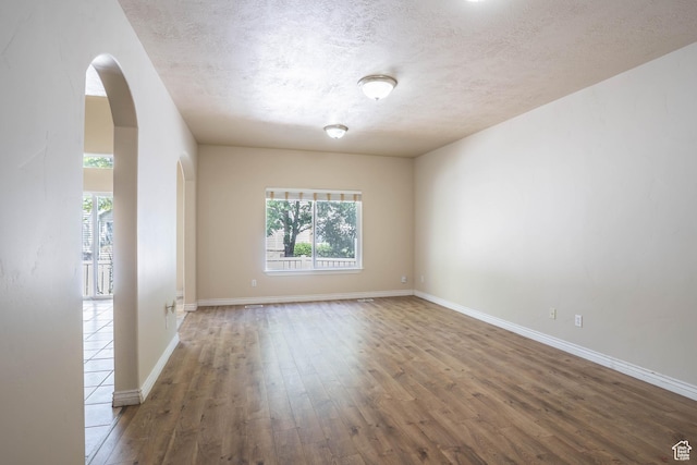 empty room with a textured ceiling, arched walkways, baseboards, and wood finished floors