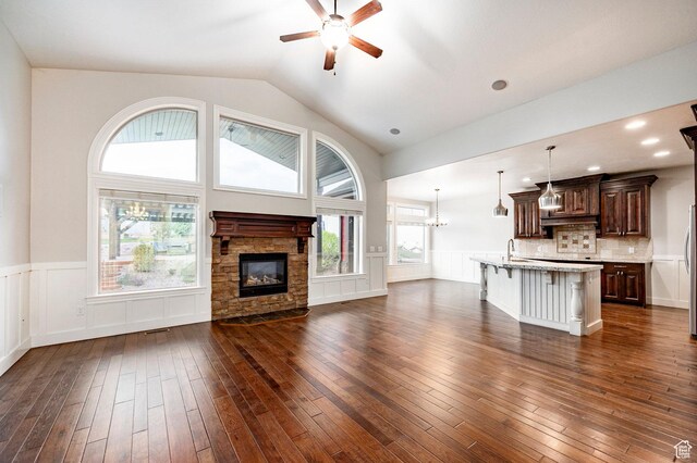 3440 Greenfield Cir, Mountain Green, UT 84050 - unfurnished living room with dark wood-style flooring, a stone fireplace, ceiling fan with notable chandelier, and a wainscoted wall