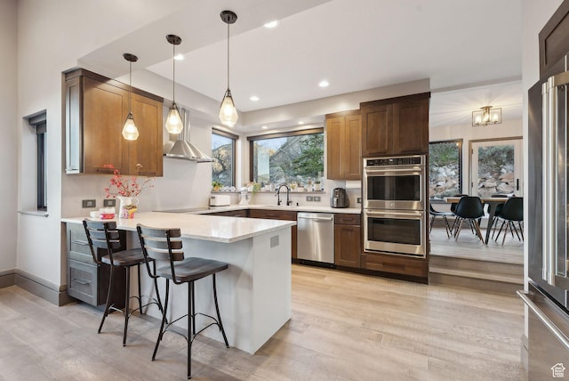 7515 Stagecoach Dr, Park City, UT 84098 - kitchen with appliances with stainless steel finishes, a peninsula, light wood-style flooring, wall chimney exhaust hood, and pendant lighting