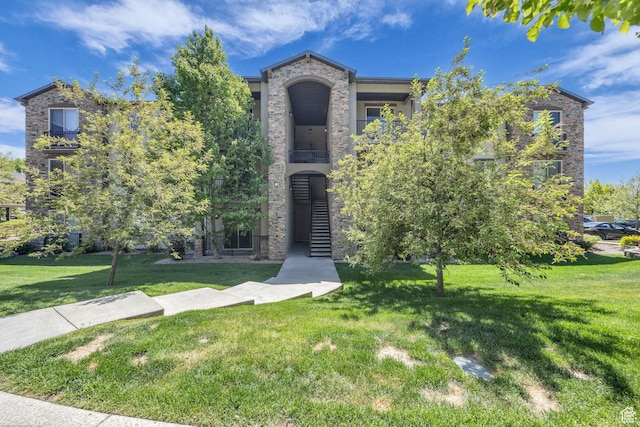 view of front of property with a balcony, stone siding, and a front yard