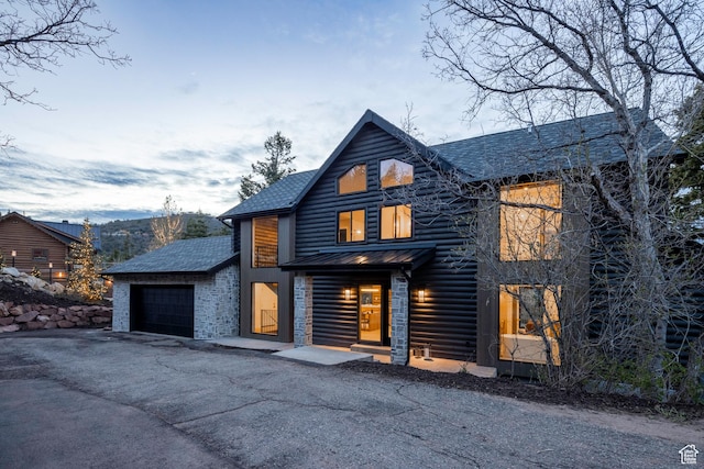 view of front of house with stone siding, an attached garage, metal roof, driveway, and a standing seam roof