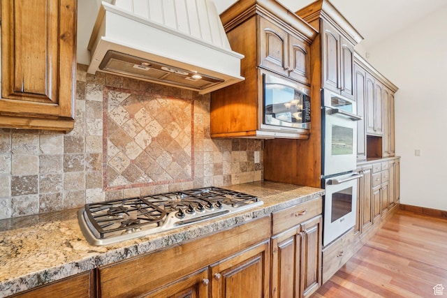 12221 Ross Creek Dr Unit 137, Kamas, UT 84036 - kitchen with light wood-type flooring, brown cabinets, premium range hood, and appliances with stainless steel finishes