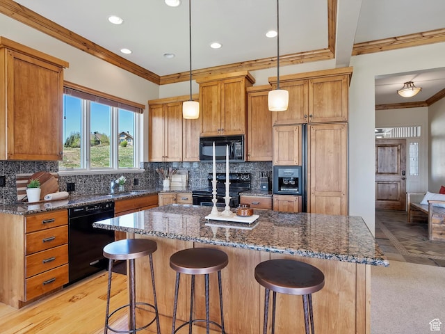 kitchen with a center island, dark stone countertops, a breakfast bar, black appliances, and ornamental molding