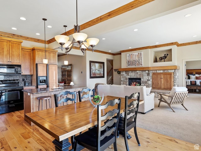 dining room with a stone fireplace, ornamental molding, light wood finished floors, and recessed lighting