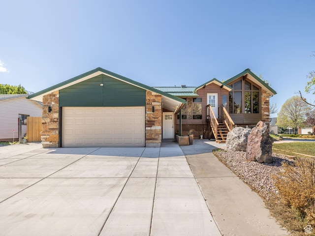 view of front of house featuring metal roof, a garage, stone siding, and driveway