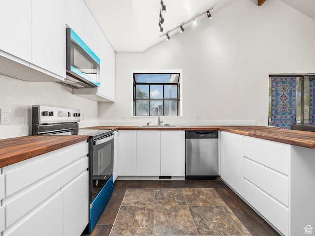 kitchen with a sink, wood counters, white cabinets, appliances with stainless steel finishes, and vaulted ceiling