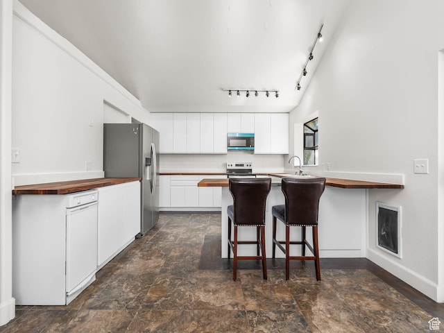 kitchen featuring a peninsula, a breakfast bar, rail lighting, white cabinets, and appliances with stainless steel finishes