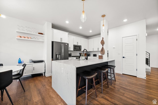 kitchen featuring dark wood-type flooring, a kitchen bar, decorative backsplash, white cabinets, and appliances with stainless steel finishes