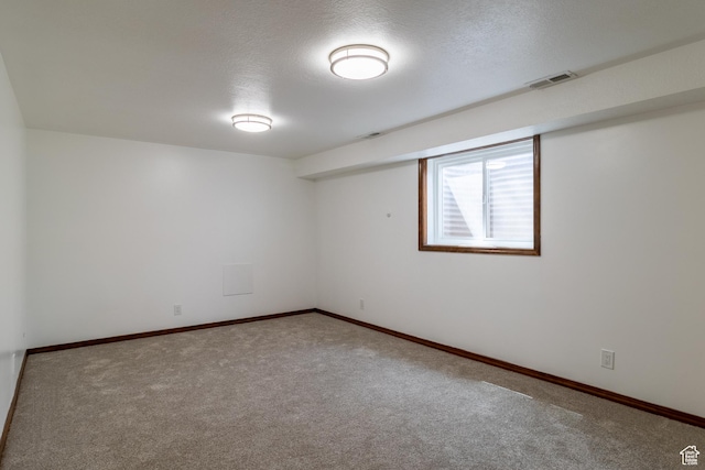 empty room with carpet flooring, a textured ceiling, visible vents, and baseboards