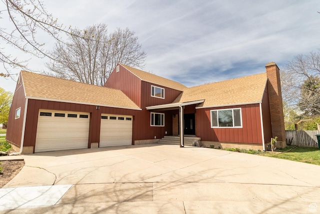 traditional-style house featuring roof with shingles, fence, concrete driveway, a garage, and a chimney