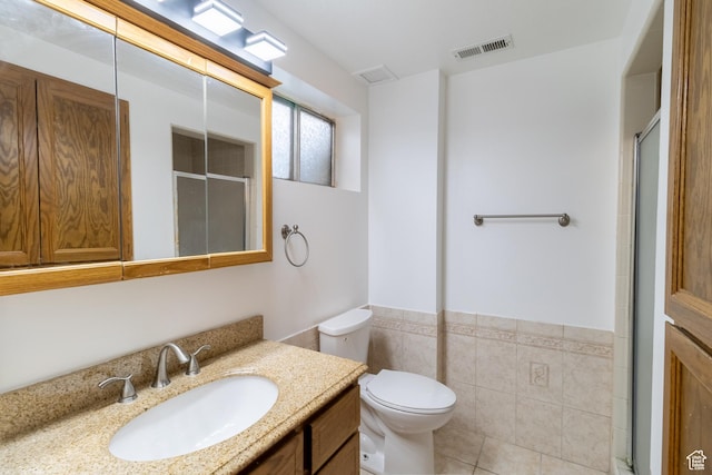 bathroom featuring tile walls, toilet, a wainscoted wall, visible vents, and a shower stall
