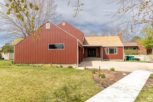 view of front of house with concrete driveway, board and batten siding, roof with shingles, and a front lawn