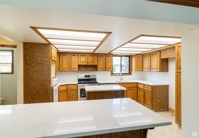 kitchen with brown cabinets, a sink, stainless steel gas range oven, light countertops, and light tile patterned flooring