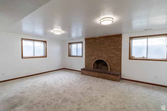 unfurnished living room featuring carpet flooring, a textured ceiling, and a brick fireplace