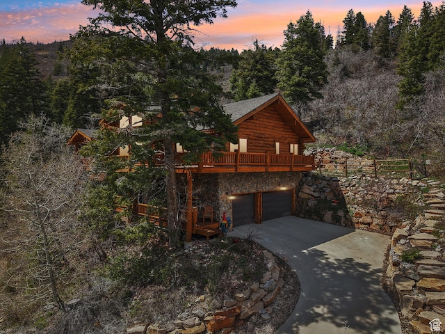exterior space featuring a deck, stone siding, driveway, a garage, and log exterior