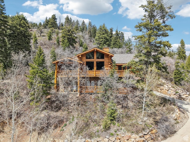 exterior space with a forest view, a chimney, log exterior, and a balcony