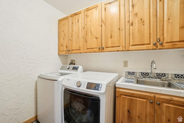 washroom featuring a sink, washer and dryer, cabinet space, and a textured wall