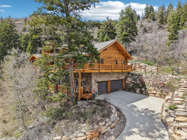 view of home's exterior featuring stone siding, an attached garage, log siding, a deck, and driveway
