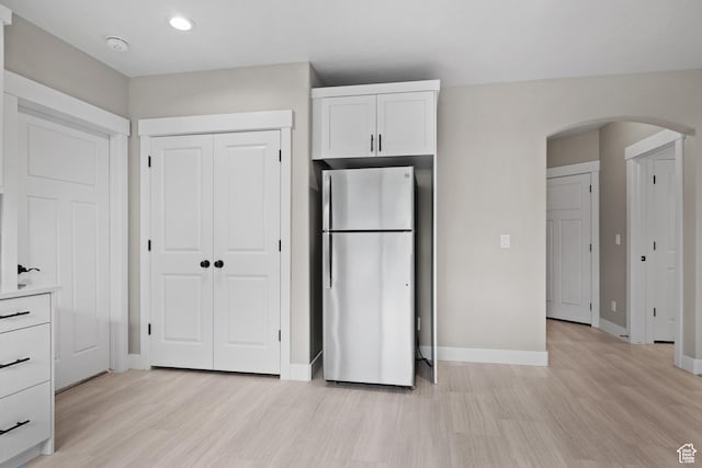 kitchen featuring freestanding refrigerator, light wood-style flooring, arched walkways, white cabinets, and baseboards