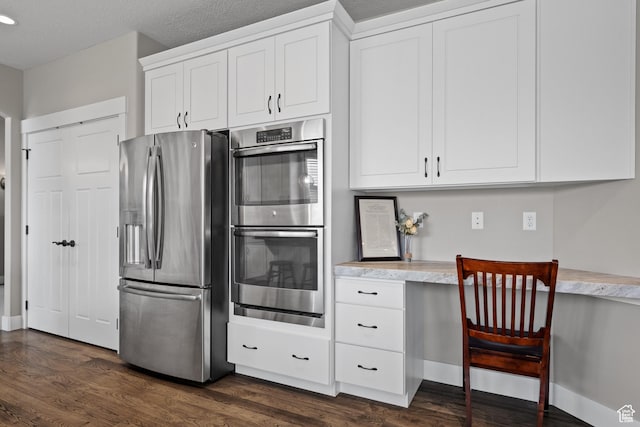 kitchen with built in study area, white cabinets, dark wood-style floors, and appliances with stainless steel finishes