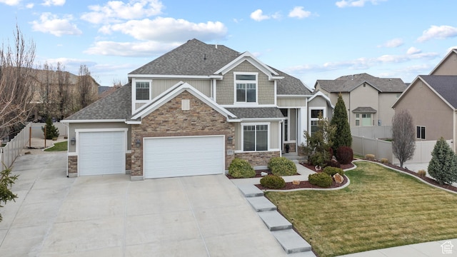 craftsman inspired home featuring roof with shingles, fence, stone siding, concrete driveway, and a front lawn