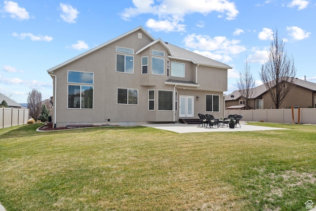 rear view of property featuring fence, stucco siding, a patio area, and a lawn