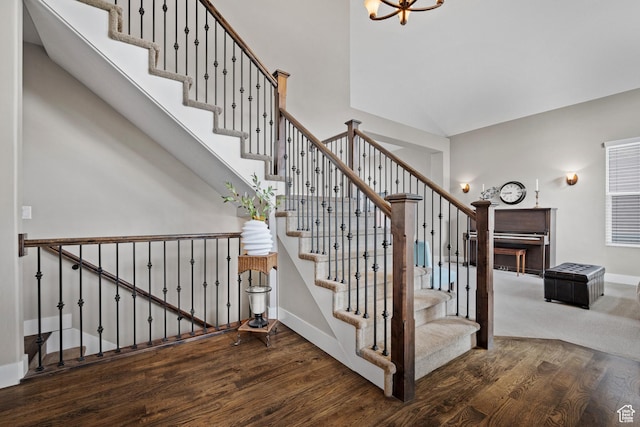 stairway featuring a towering ceiling, an inviting chandelier, wood finished floors, and baseboards