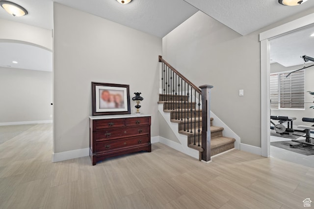 stairs featuring a textured ceiling, baseboards, arched walkways, and wood finished floors