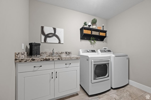 clothes washing area with a sink, cabinet space, a textured ceiling, washer and dryer, and baseboards