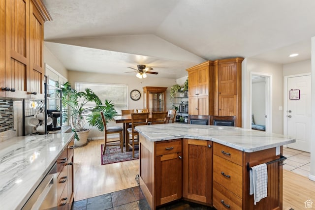 kitchen with a ceiling fan, lofted ceiling, a center island, light stone counters, and tasteful backsplash