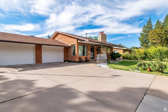 ranch-style home featuring an attached garage, a chimney, concrete driveway, a front lawn, and brick siding