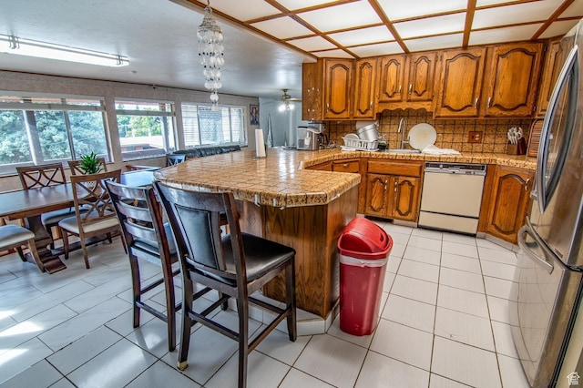 kitchen with brown cabinetry, a peninsula, freestanding refrigerator, and dishwasher