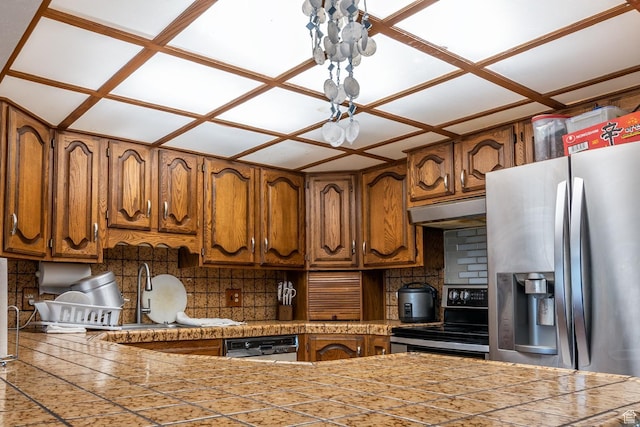 kitchen with a sink, brown cabinetry, under cabinet range hood, appliances with stainless steel finishes, and decorative backsplash