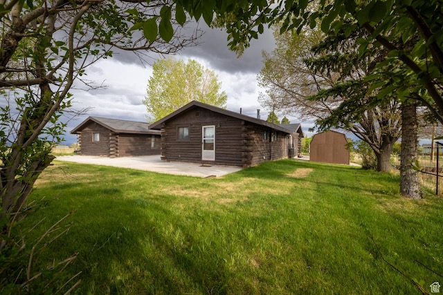 back of property featuring log siding, a patio, an outdoor structure, and a shed