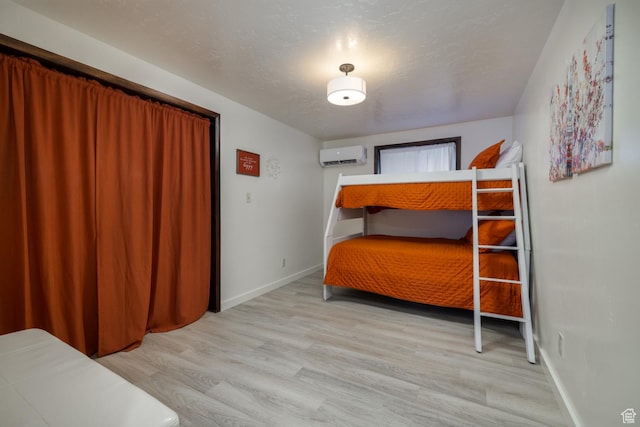 bedroom with a wall mounted air conditioner, wood finished floors, and baseboards