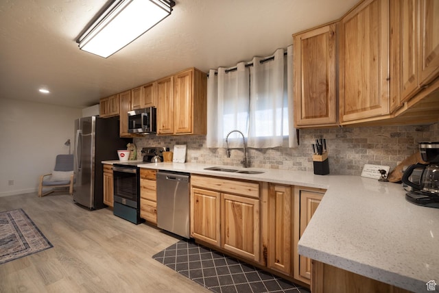 kitchen with appliances with stainless steel finishes, a sink, tasteful backsplash, light wood-style flooring, and baseboards