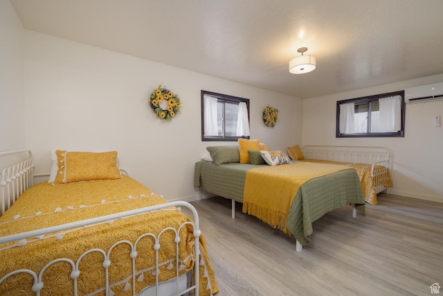 bedroom with a wall mounted air conditioner, wood finished floors, and baseboards