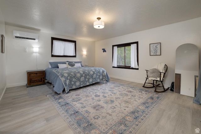 bedroom featuring light wood-style floors, an AC wall unit, and baseboards