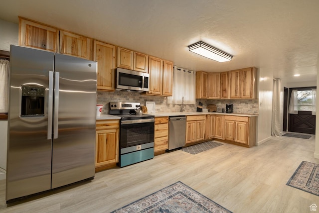 kitchen with appliances with stainless steel finishes, light countertops, light wood-type flooring, backsplash, and light brown cabinets