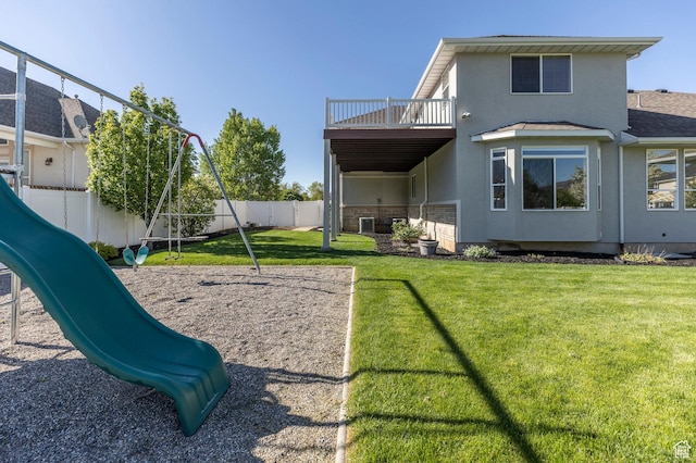 rear view of house with playground community, stucco siding, fence, a lawn, and a balcony