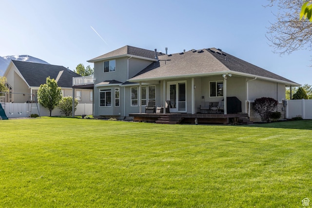 rear view of property with a yard, stucco siding, fence, and a wooden deck