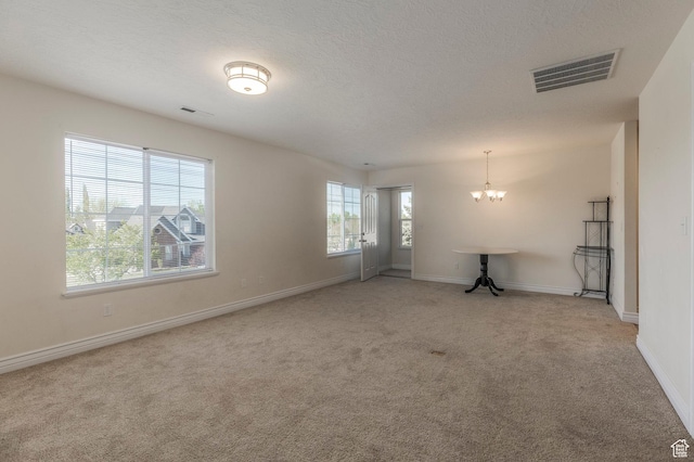 empty room with baseboards, a notable chandelier, visible vents, and light colored carpet