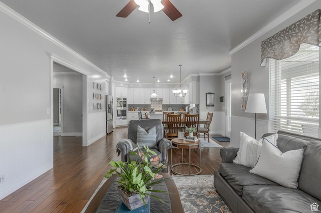 living room featuring wainscoting, ornamental molding, ceiling fan with notable chandelier, and hardwood / wood-style floors