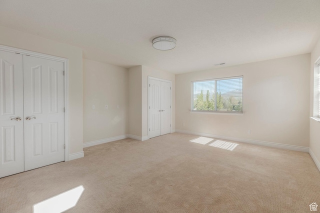 unfurnished bedroom featuring two closets, carpet, and baseboards