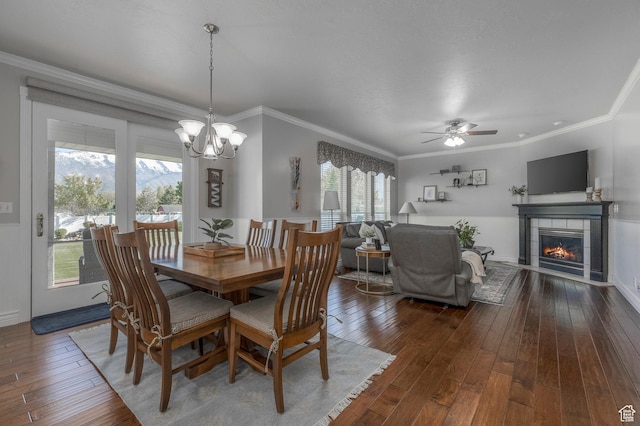 dining area featuring ornamental molding, dark wood finished floors, a fireplace, and ceiling fan with notable chandelier