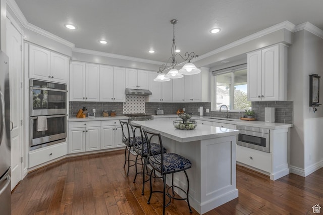 kitchen featuring stainless steel appliances, a kitchen breakfast bar, under cabinet range hood, and white cabinets